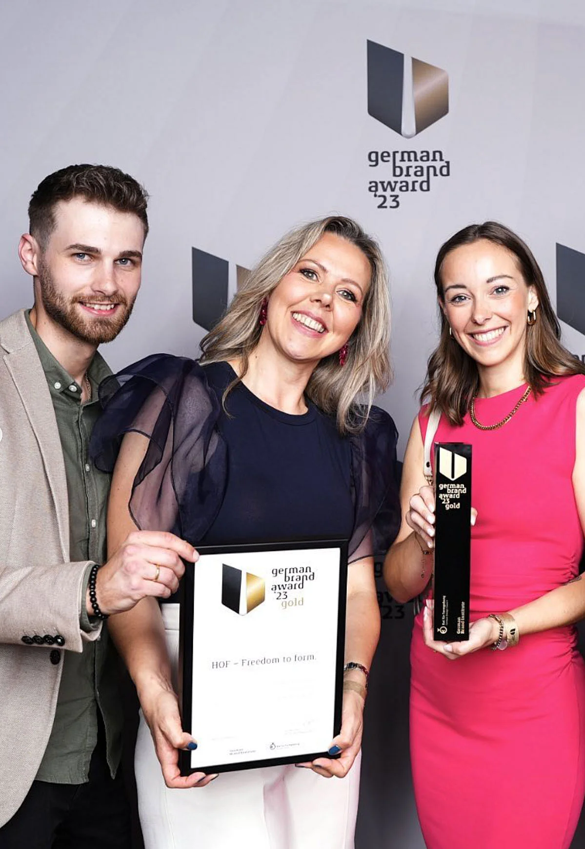 Drei Personen mit Urkunde und Preis Drei Personen halten eine Urkunde und einen Preis vor einem Hintergrund mit dem Logo "German Brand Award 23".