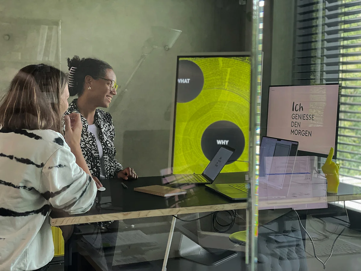 Zwei Personen arbeiten in einem modernen Büro Zwei Personen stehen an einem Tisch mit Laptops und Monitoren in einem modernen Raum. Bildschirm zeigt Text.